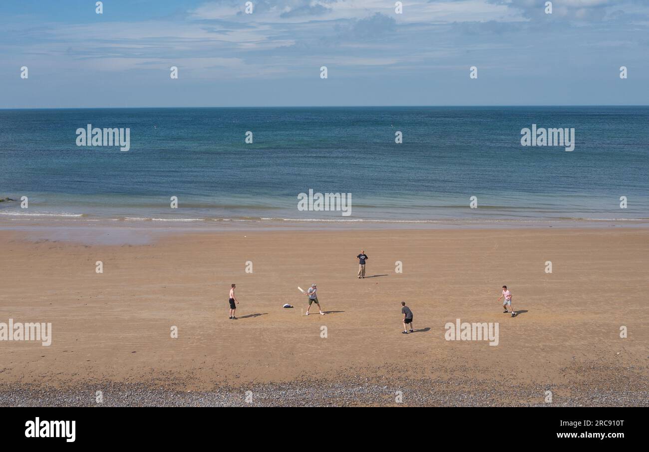 Five young men playing cricket on the beach at low tide at Sheringham