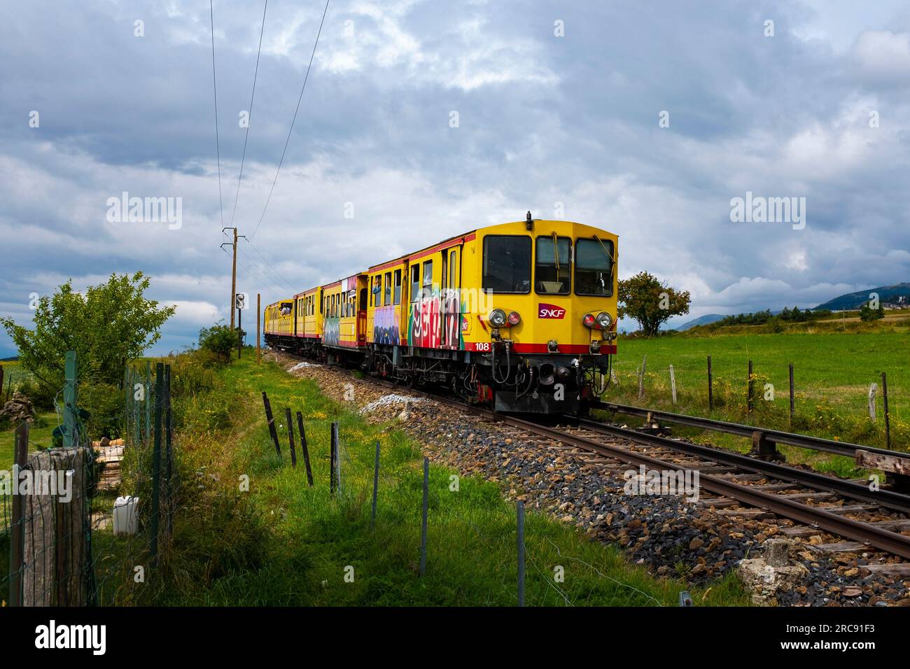 The Train Jaune, Yellow Train, Canari, or Ligne de Cerdagne, crosses the Route National 116 road. The train negotiates a 63km long railway from Villef Stock Photo