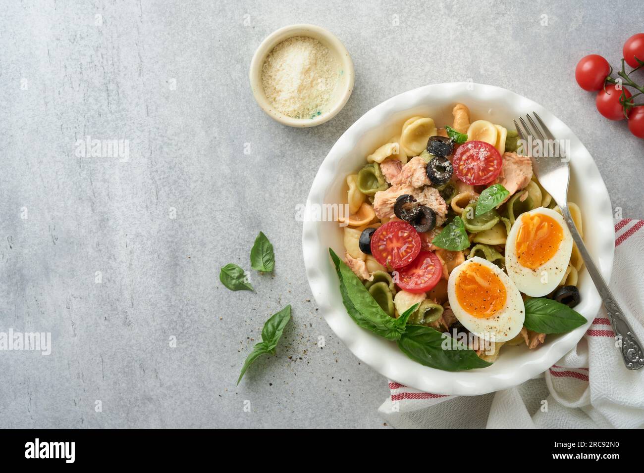 Italian pasta salad. Orecchiette pasta with tuna, tomato cherry, olive, basil and parmesan cheese in plate on grey stone or concrete background. Tradi Stock Photo