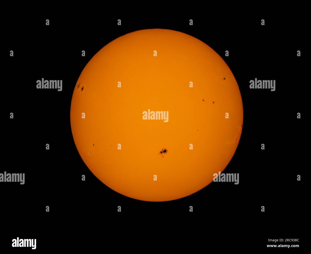 The orange coloured afternoon sun glowing with many sunspots using a homemade solar filter. Stock Photo