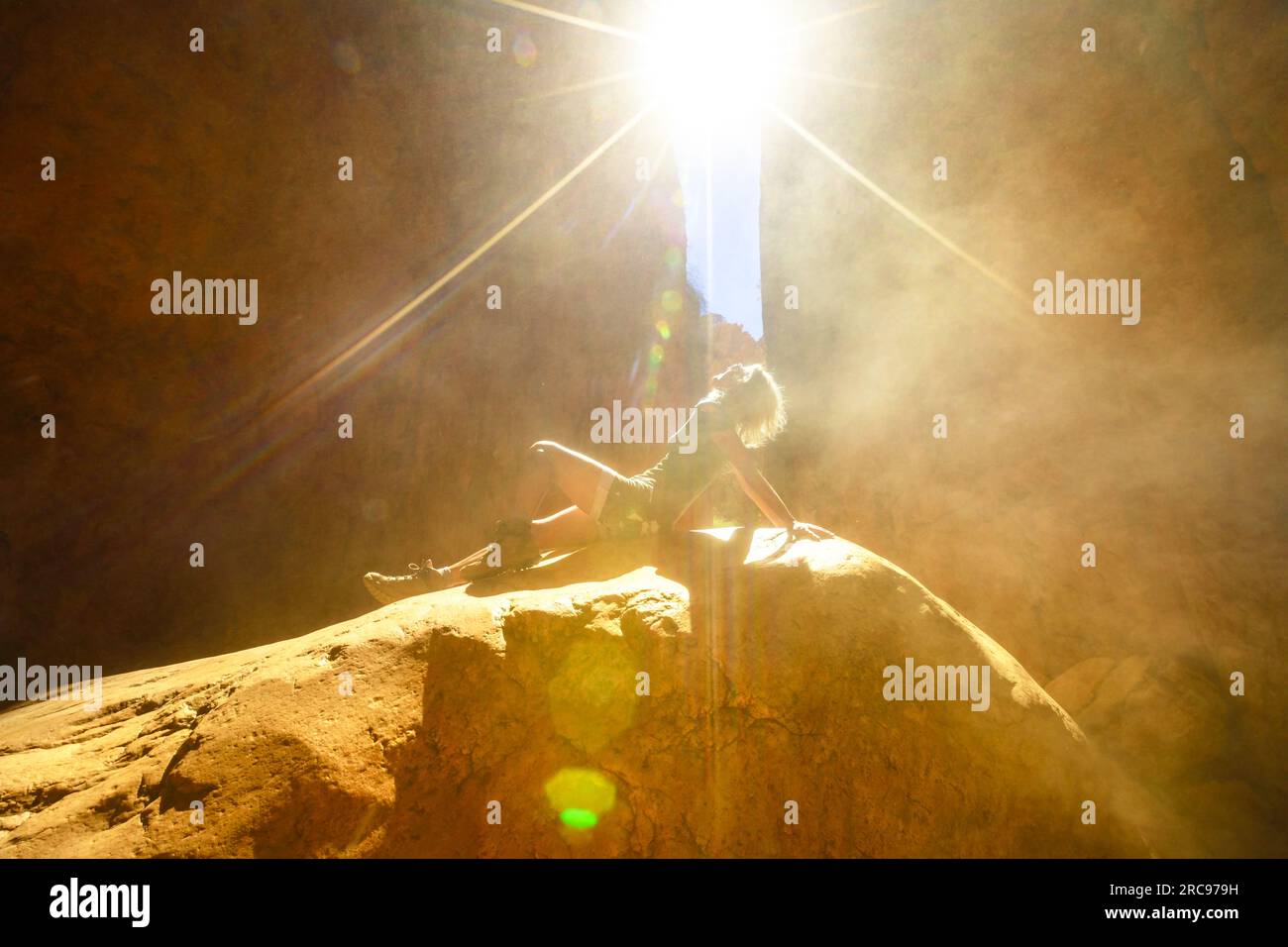 Tourist woman sitting on a rock with light sun effects with sand flying in the natural gorge of Standley Chasm, West MacDonnell Ranges. Australian Stock Photo
