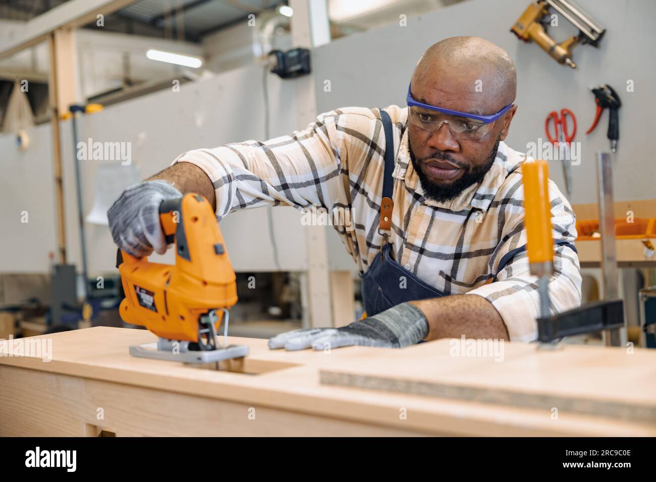 black african male carpenter joiner using Jig Saw wood panel cutter to cut making furniture panel in workshop Stock Photo