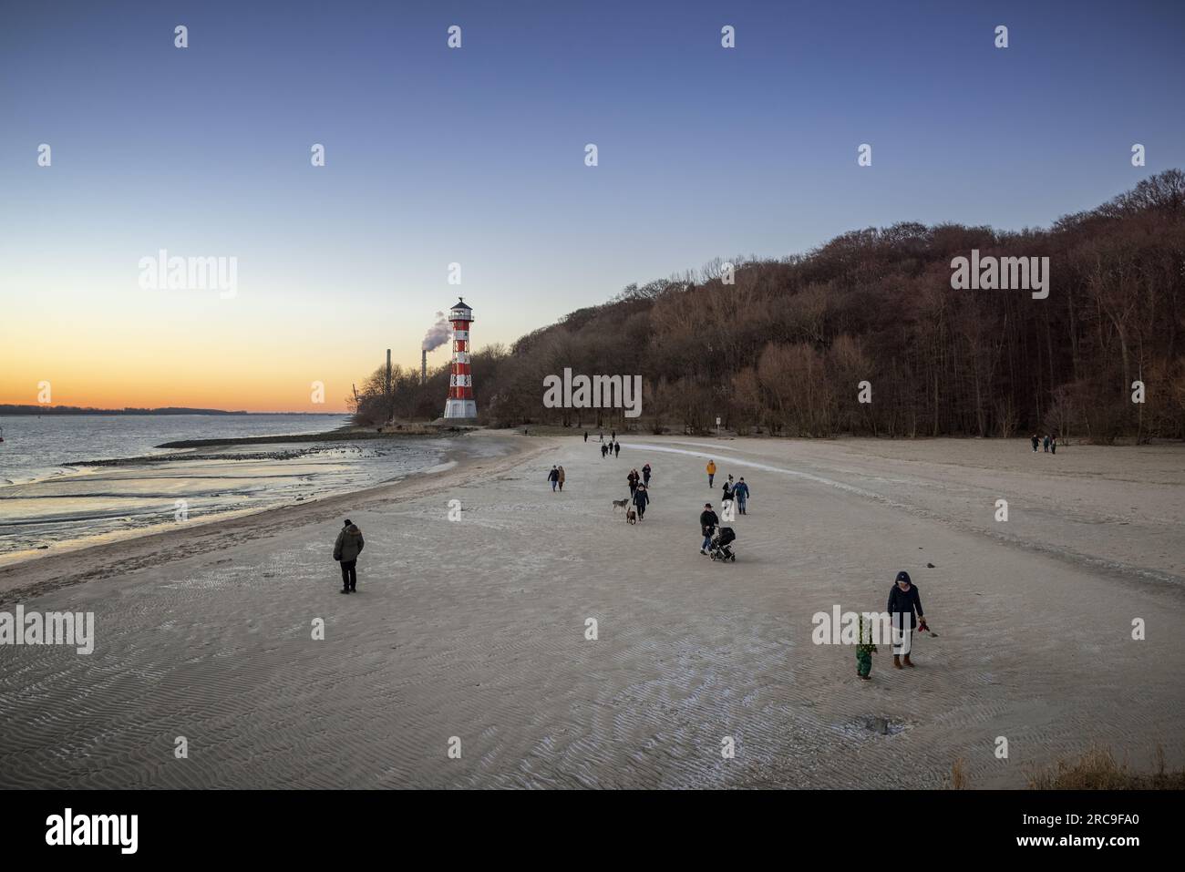 Eisiger Winternachmittag am Strand von Wittenbergen in Hamburg-Rissen. Die untergehende Sonne beleuchtet den Leuchtturm. Im Hintergrund die Schornstei Stock Photo