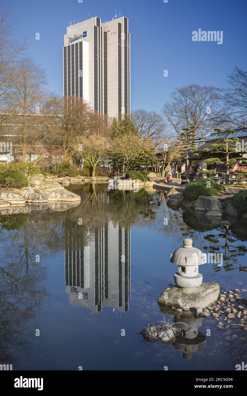 Blick vom japanischen Garten in Planten un Blomen auf das Radisson-Hotel am Hamburger Dammtor. Das Hochhaus-Fassade spiegelt sich im Teich Stock Photo