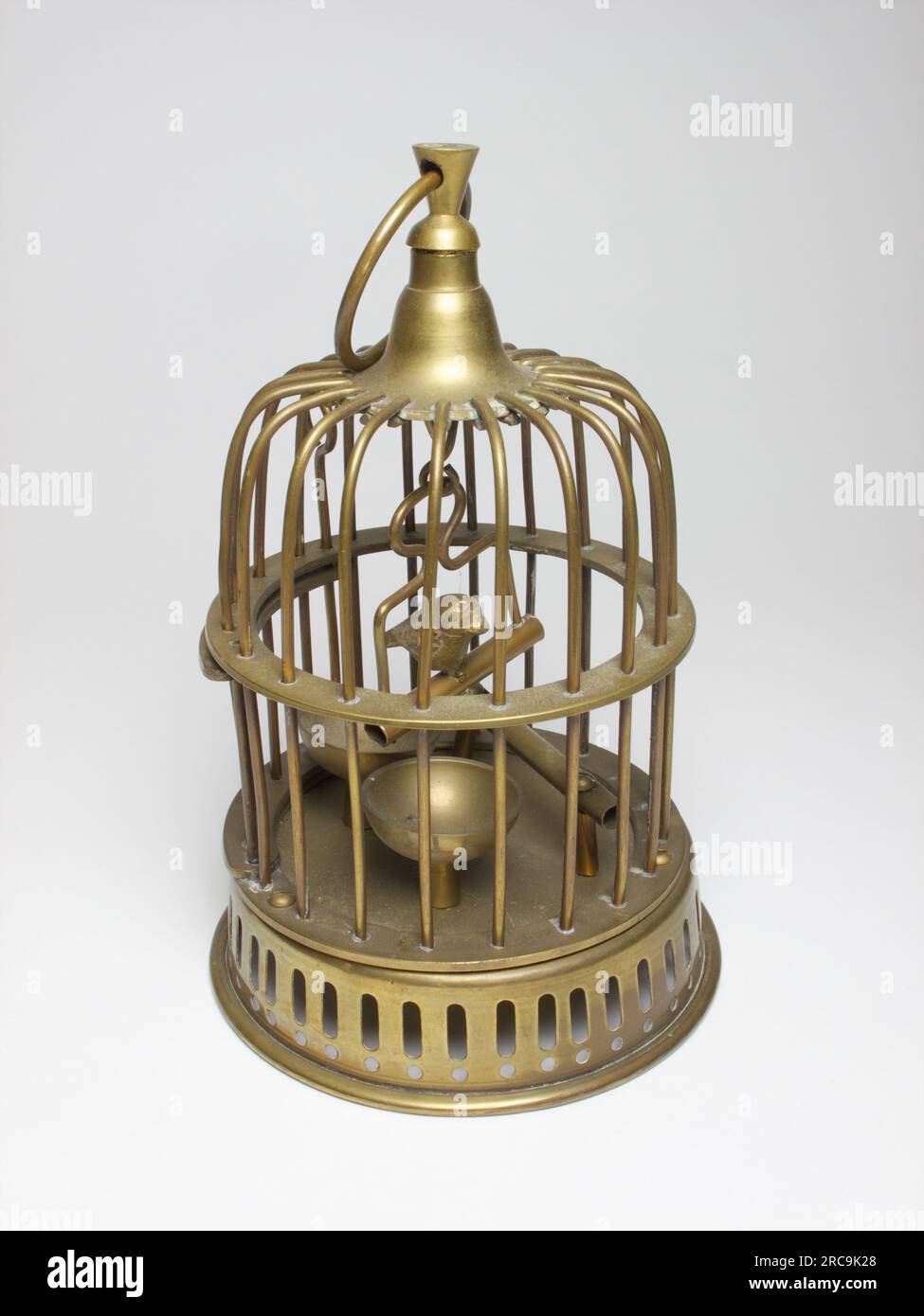 Vintage miniature brass bird cage with opening door and a with a bird sitting on a swing. The cage measures approximately 17.5cm high. The photographs Stock Photo