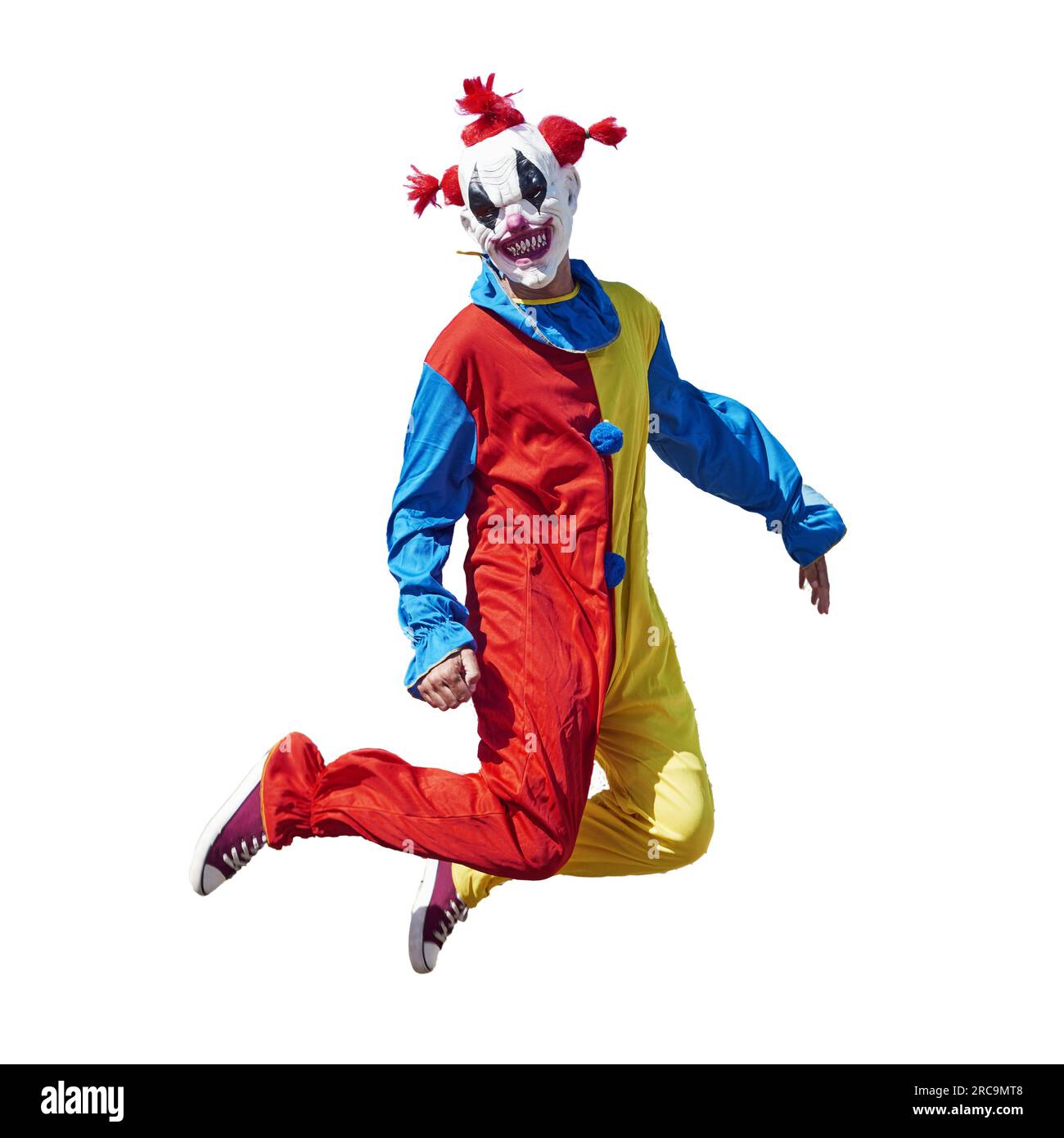 a scary clown wearing a colorful yellow, red and blue costume, jumping on a white background Stock Photo