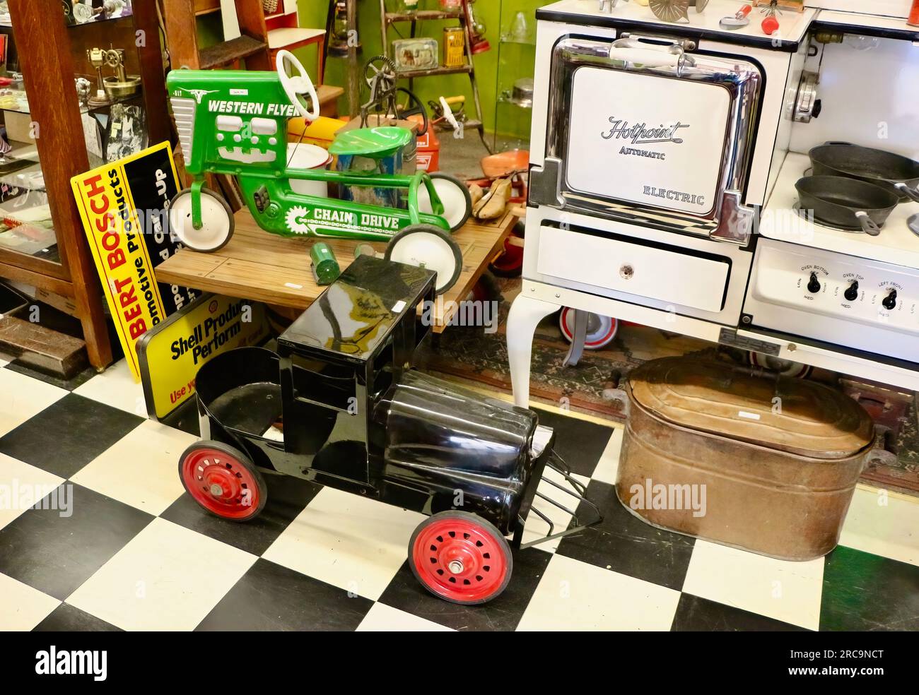 Photo of a black train and green tractor pedal cars and a vintage Hotpoint stove for sale in an antiques shop in Snohomish Washington State USA Stock Photo