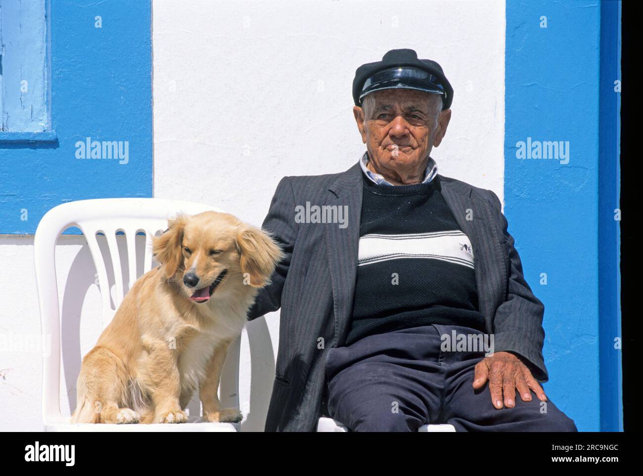 Griechenland, Karpathos, Arkasa (Arkassa), Mann mit Hund sitzt vor Kafenion Stock Photo