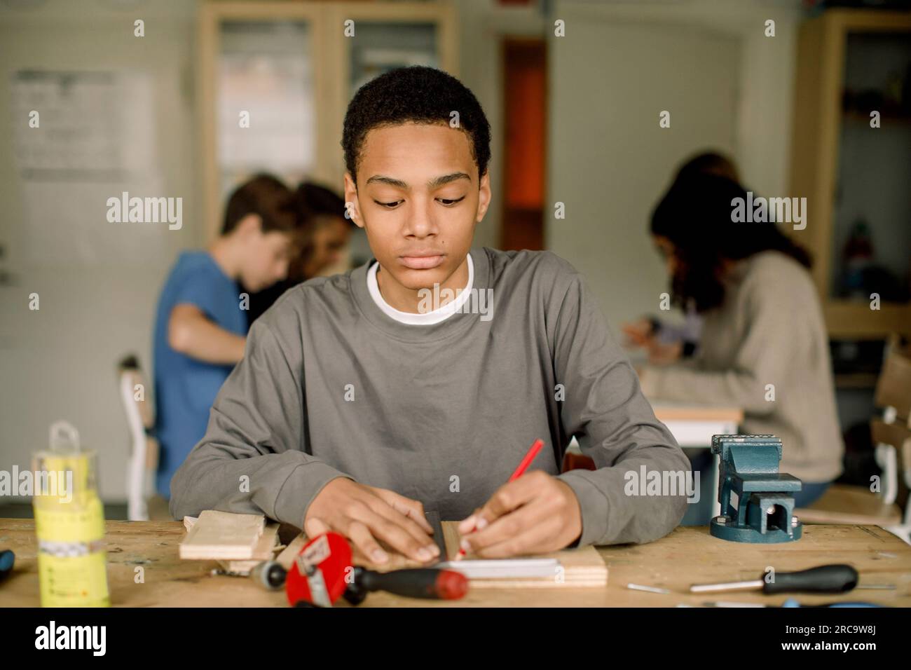 Focused male teenage student measuring wood during carpentry class at