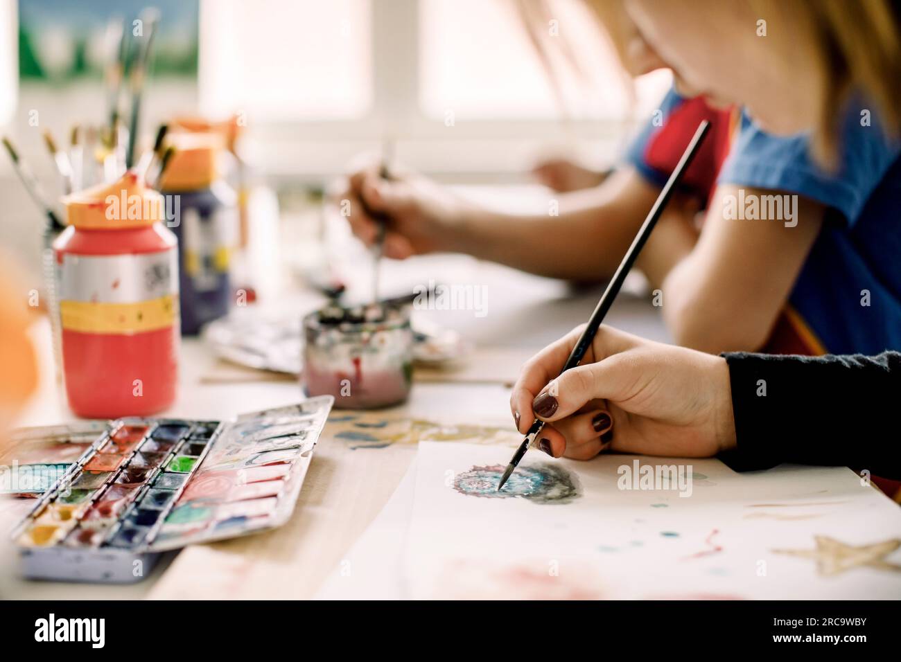 Hand of female teenage student painting on paper with brush during art