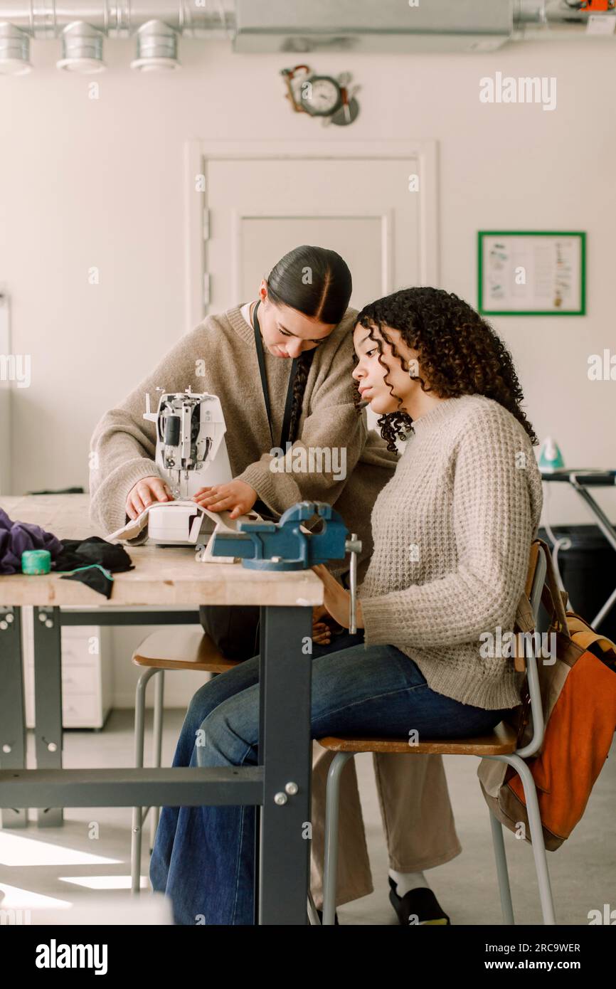 Teacher assisting female student looking at sewing machine in art class at high school Stock Photo