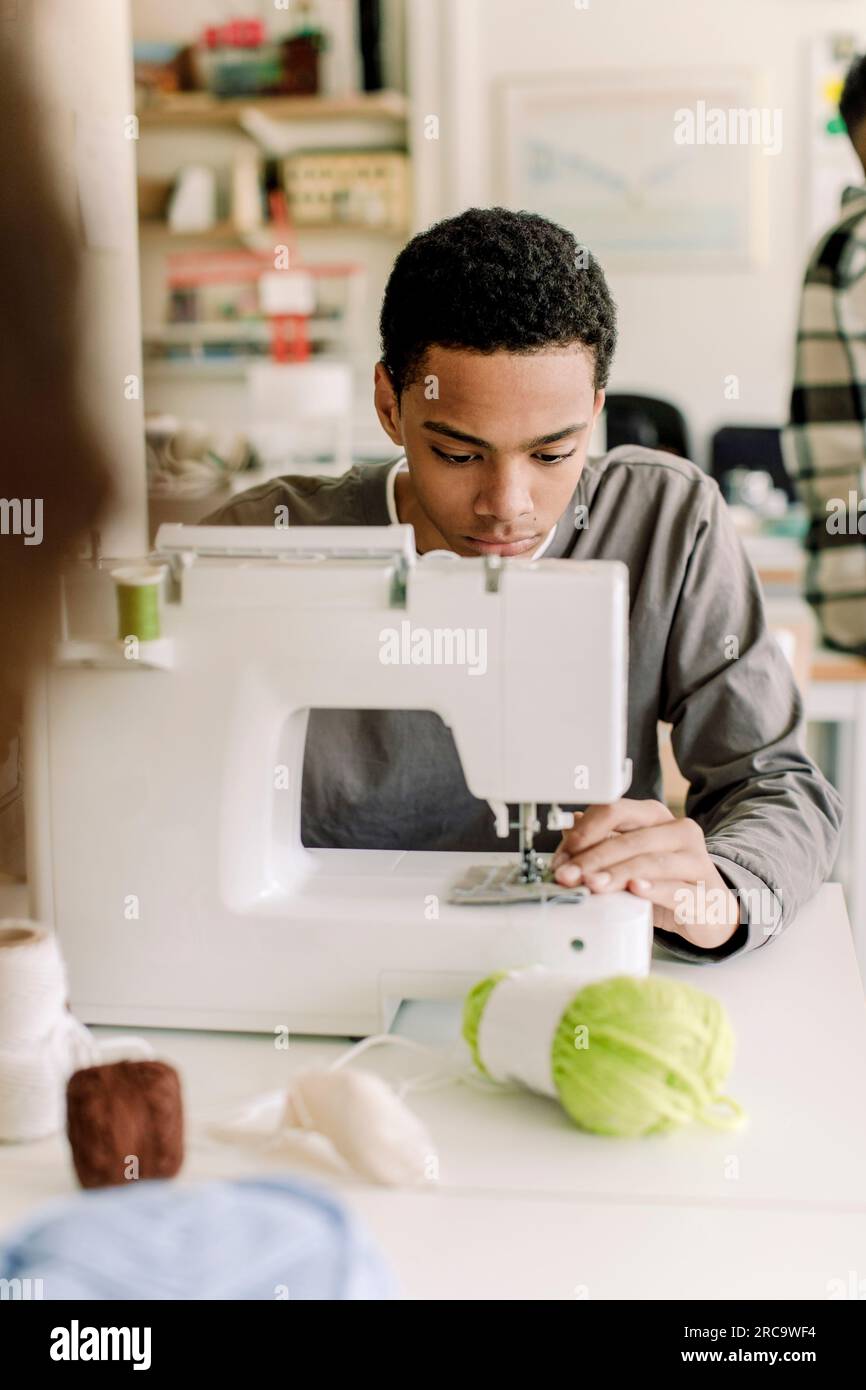 Focused teenage male student using sewing machine in art class at high school Stock Photo