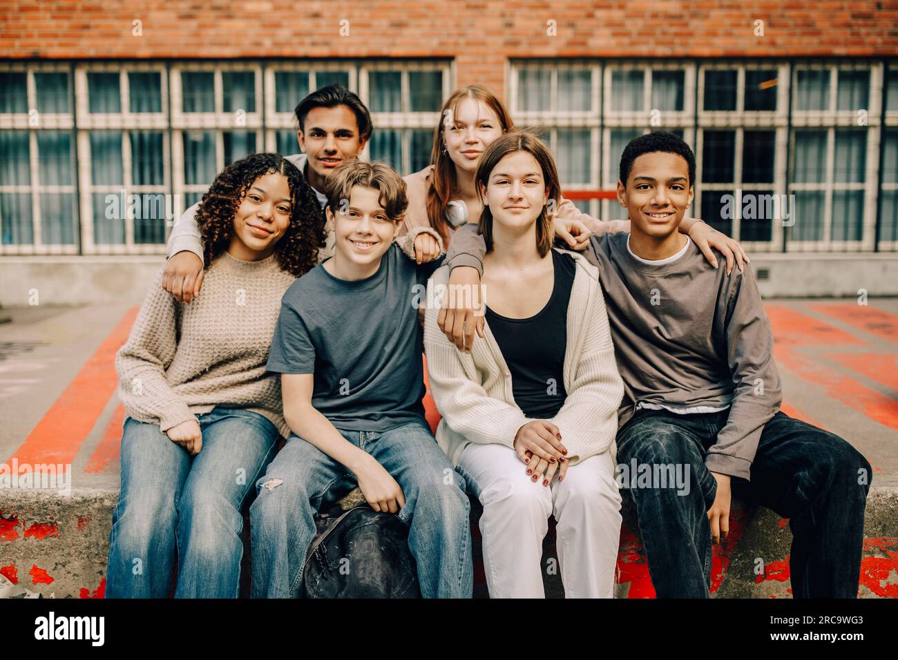 Portrait of smiling male and female students sitting with arms around ...