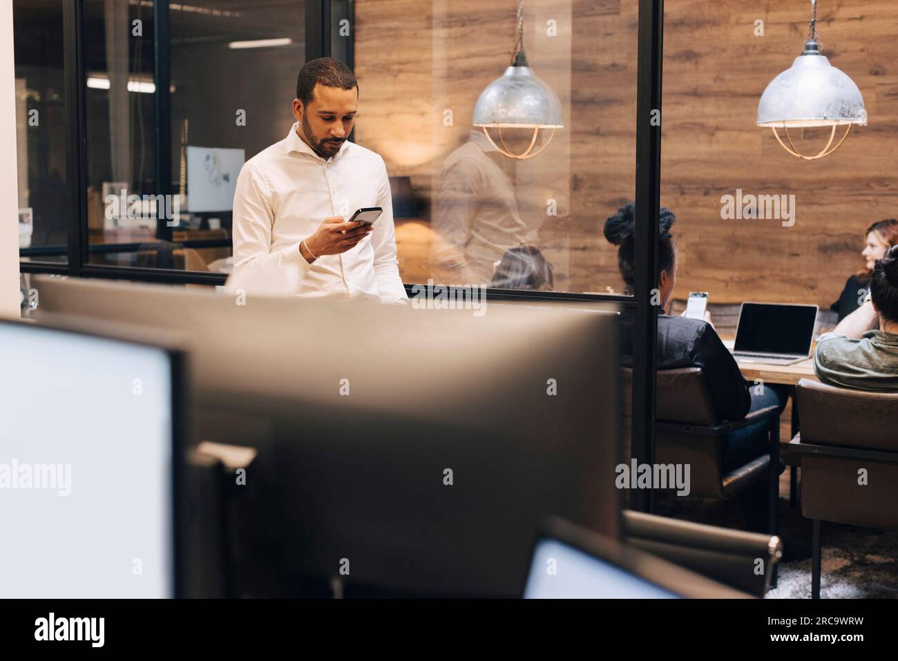 Businessman using smart phone standing at illuminated creative office Stock Photo