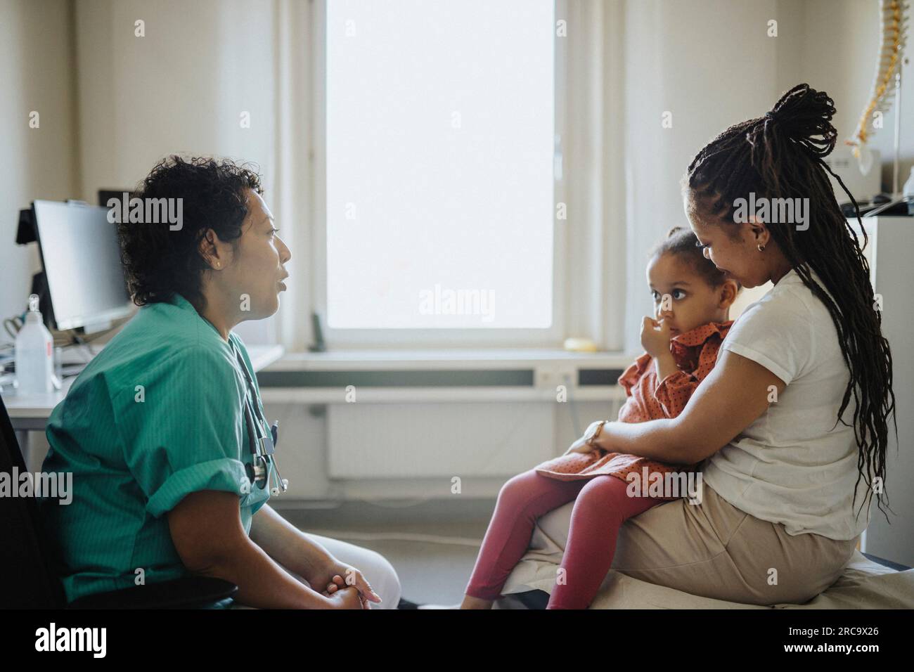 Woman carrying ill daughter discussing with pediatric in clinic Stock Photo