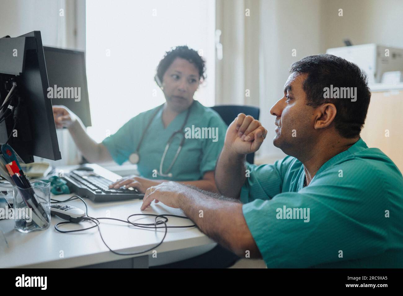 Male and female doctors discussing over computer at desk in hospital Stock Photo