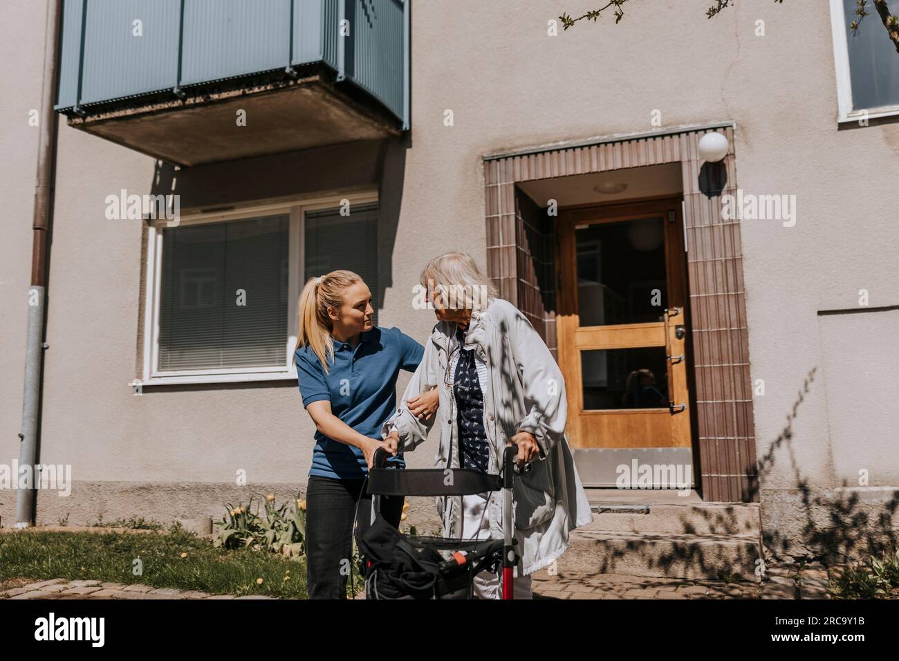 Female caregiver assisting senior woman moving out with walker Stock Photo