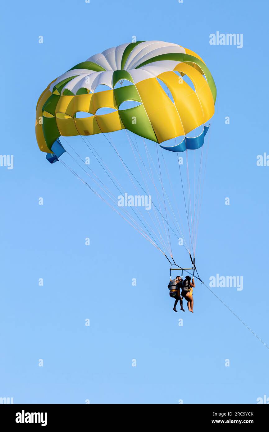 FIUMEFREDDO DI SICILIA, SICILY, ITALY - AUGUST 12, 2022 A black couple in bathing suits and life jackets pulled and flying with a yellow parachute nea Stock Photo