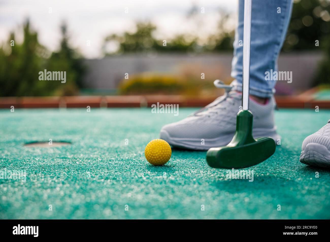 Golfer playing miniature golf and trying putting ball into hole. Leisure activity during summer Stock Photo