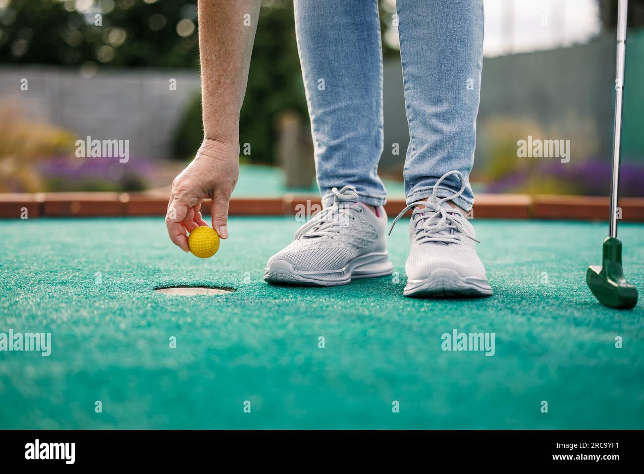 Woman plays mini golf and taking ball out from the hole after successful putting Stock Photo