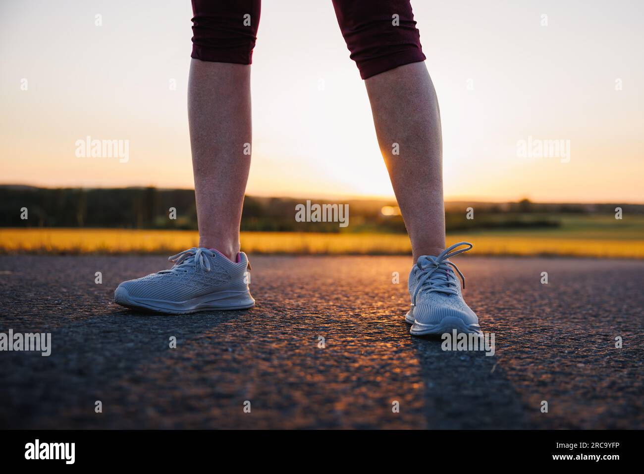 Woman with running shoe standing on road at sunset. Sport training outdoors Stock Photo