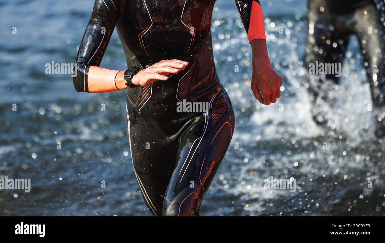 Sport person running from water after swimming part of a triathlon competition. Swimmer in neoprene wetsuit Stock Photo