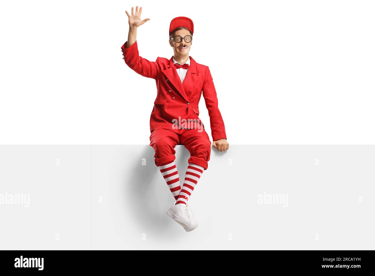 Entertainer in red suit sitting on a blank panel and waving isolated on white background Stock Photo