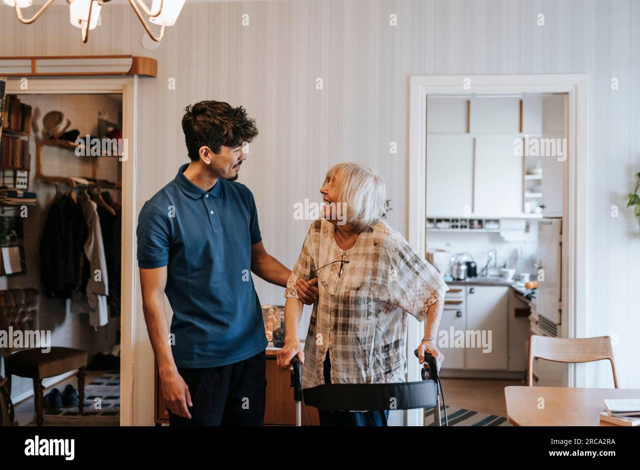 Smiling male healthcare worker talking to senior woman standing with walker at home Stock Photo