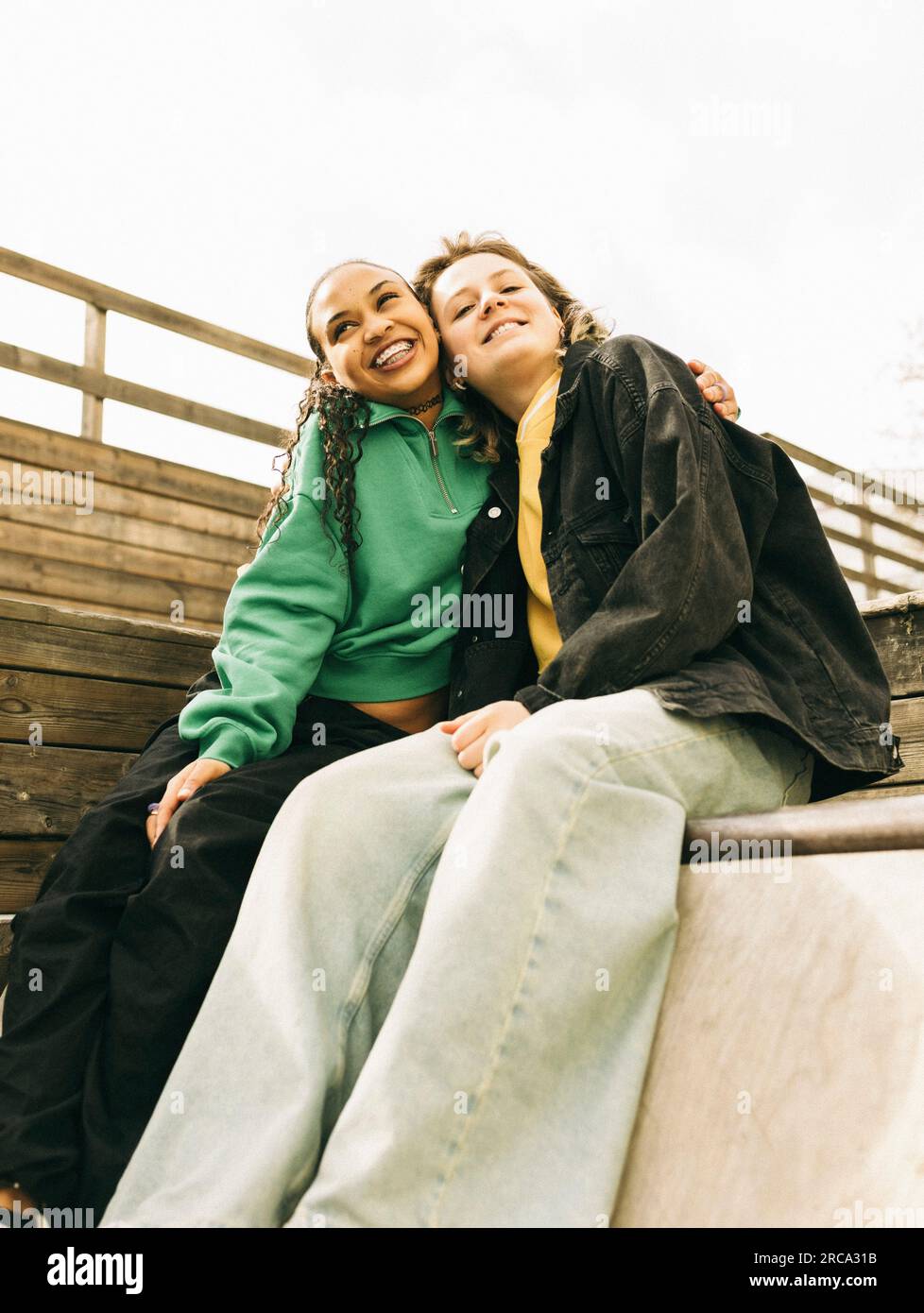 Smiling young woman embracing female friend while sitting on steps Stock Photo