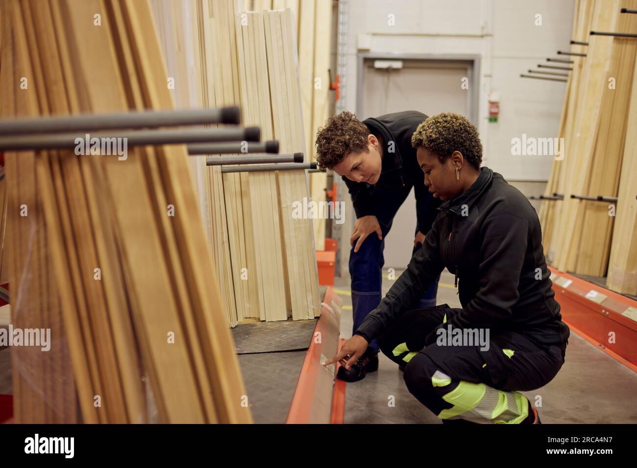 Multiracial female colleagues discussing over label in distribution warehouse of lumber industry Stock Photo