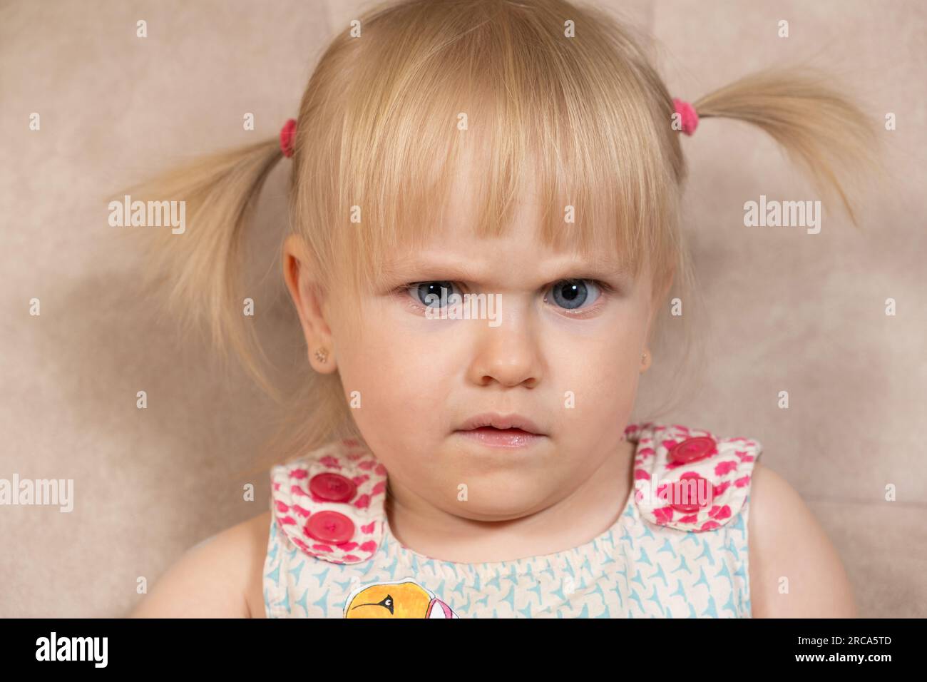 Portrait of a 2-year-old girl frowning suspiciously looking at the camera. Stock Photo