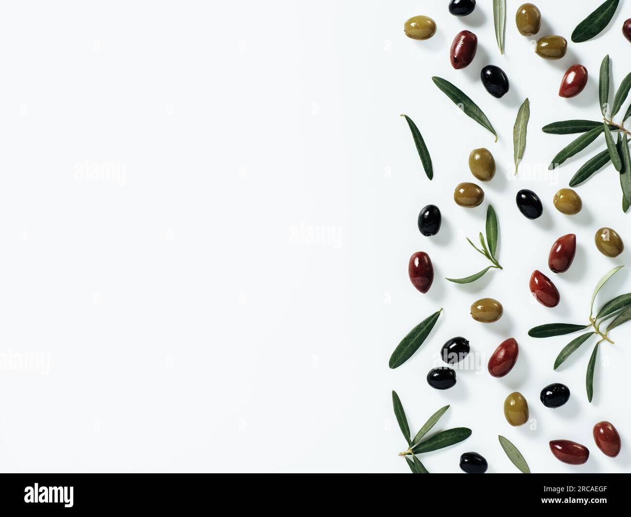 Pattern with green, black and red olives and olives tree leaves and branches on white background. Mix olive tree fruits and branches as background with copy space. Top view or flat lay. Stock Photo