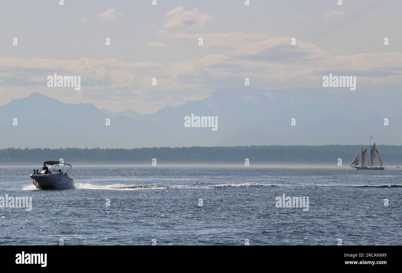 Fast moving motor boat and a distant schooner Bay Lady sailing vessel in full sail on a calm sunny afternoon Puget Sound Seattle Washington State USA Stock Photo