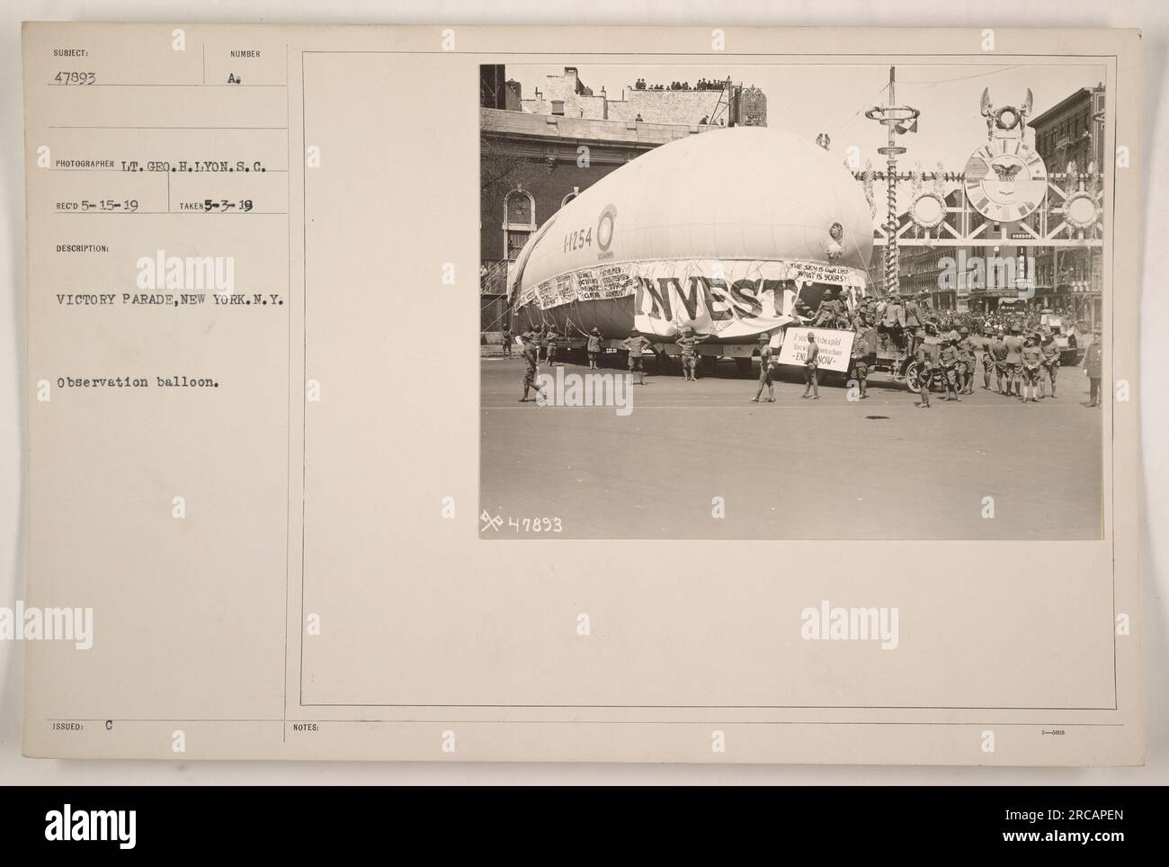 Soldiers march in a Victory Parade in New York, following the end of World War I. An observation balloon, labeled SUBIECT 47893 BECO 5-15-19, hovers above the parade. The photograph was taken by Lieutenant Geo. H. Lyon on May 3, 1919. Stock Photo