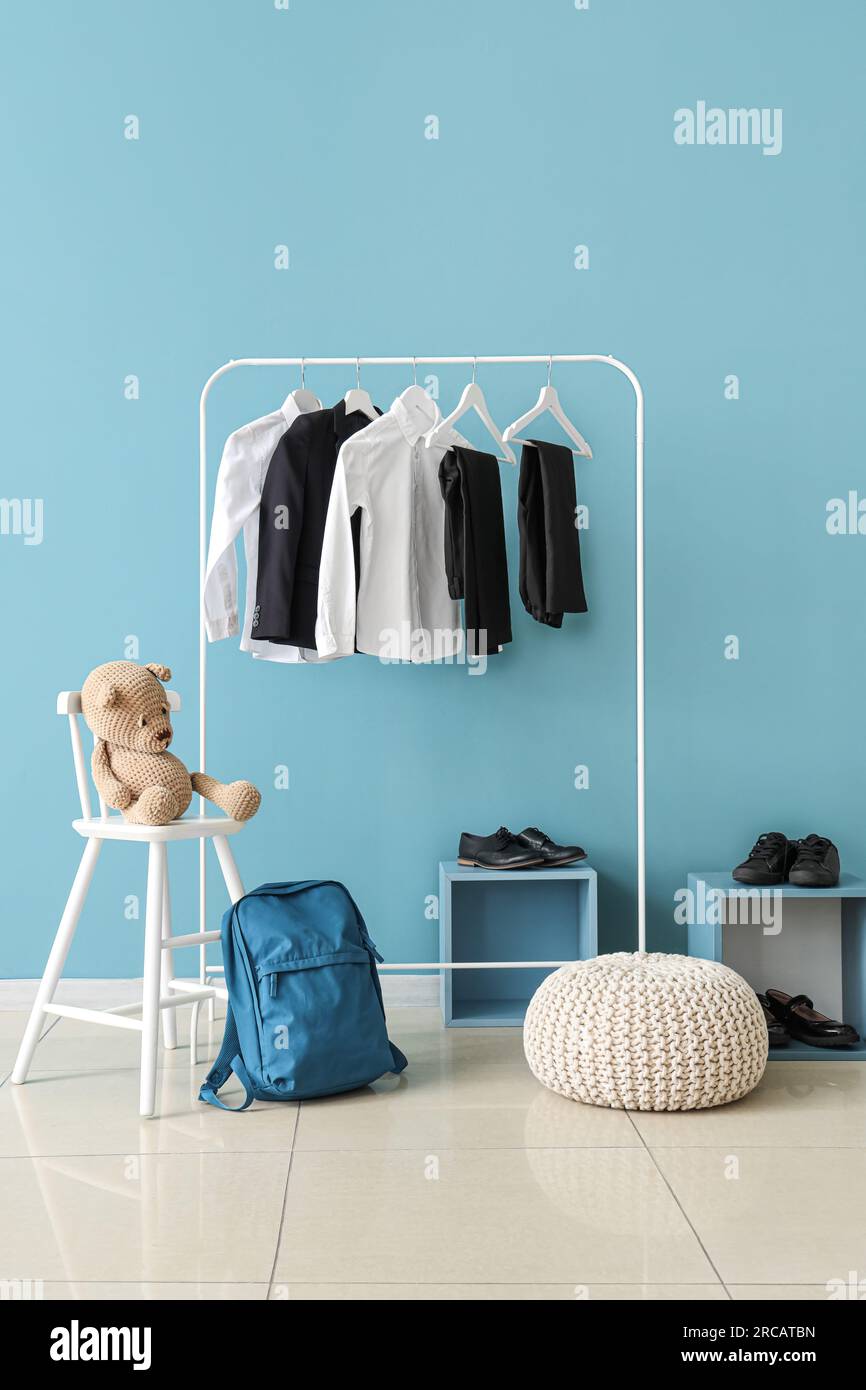 Stylish school uniform hanging on rack, backpack, shoes and pouf near blue wall in room Stock Photo