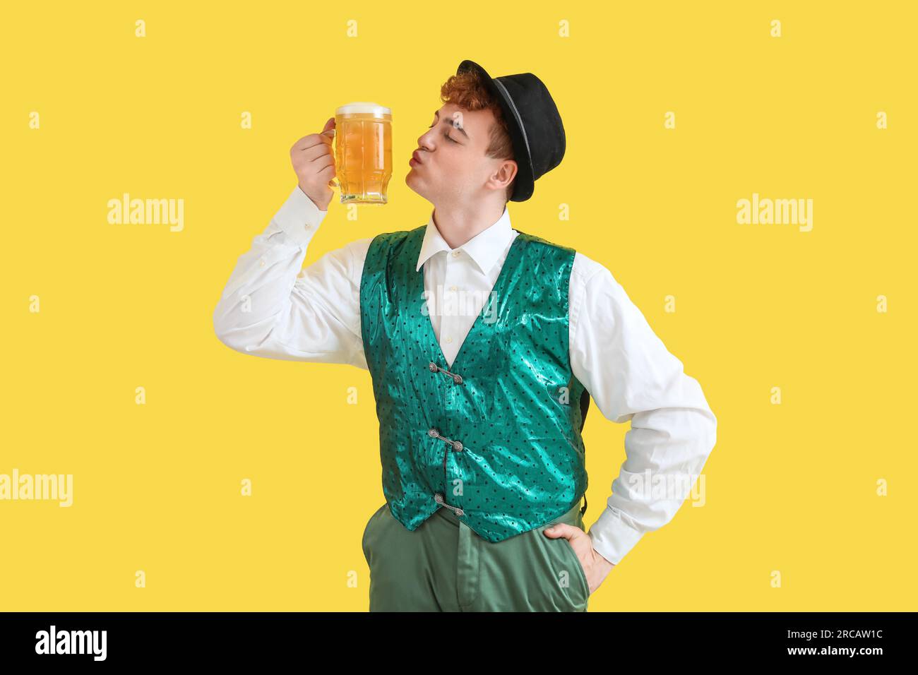 Young man in traditional German clothes with beer on yellow background