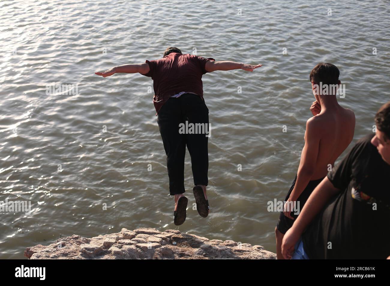 Baghdad, Iraq. 13th July, 2023. An Iraqi man dives into the water of