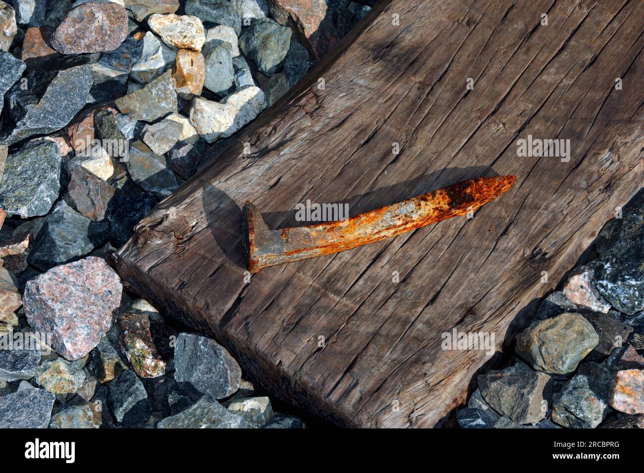 Wooden crosstie lies on bed of rock and gravel. Railroad tie has rusty