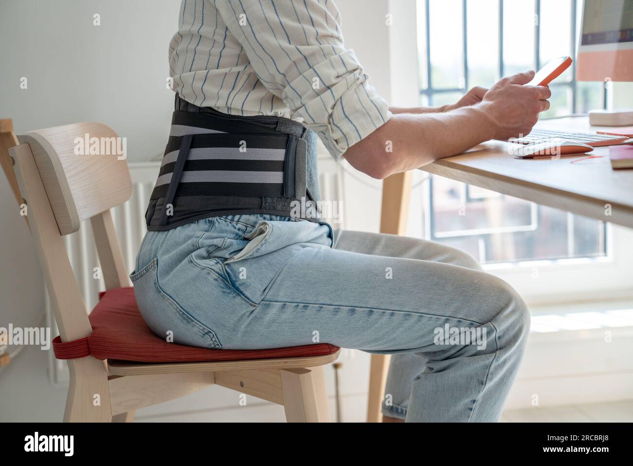 Man freelancer wearing back support belt working remotely from home Stock Photo