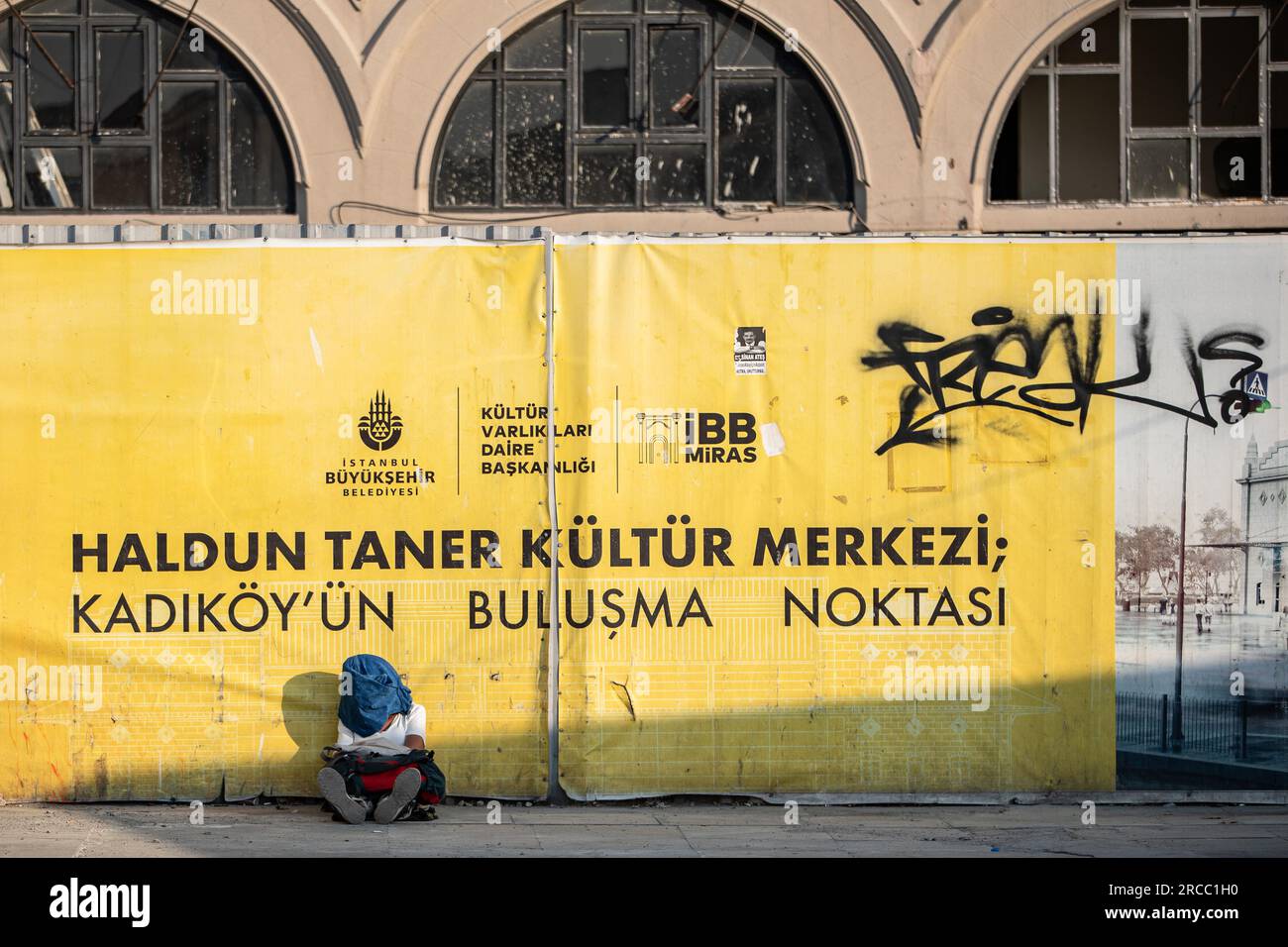 A man covers himself from the sun while sitting on the ground near the Kadikoy dock during the