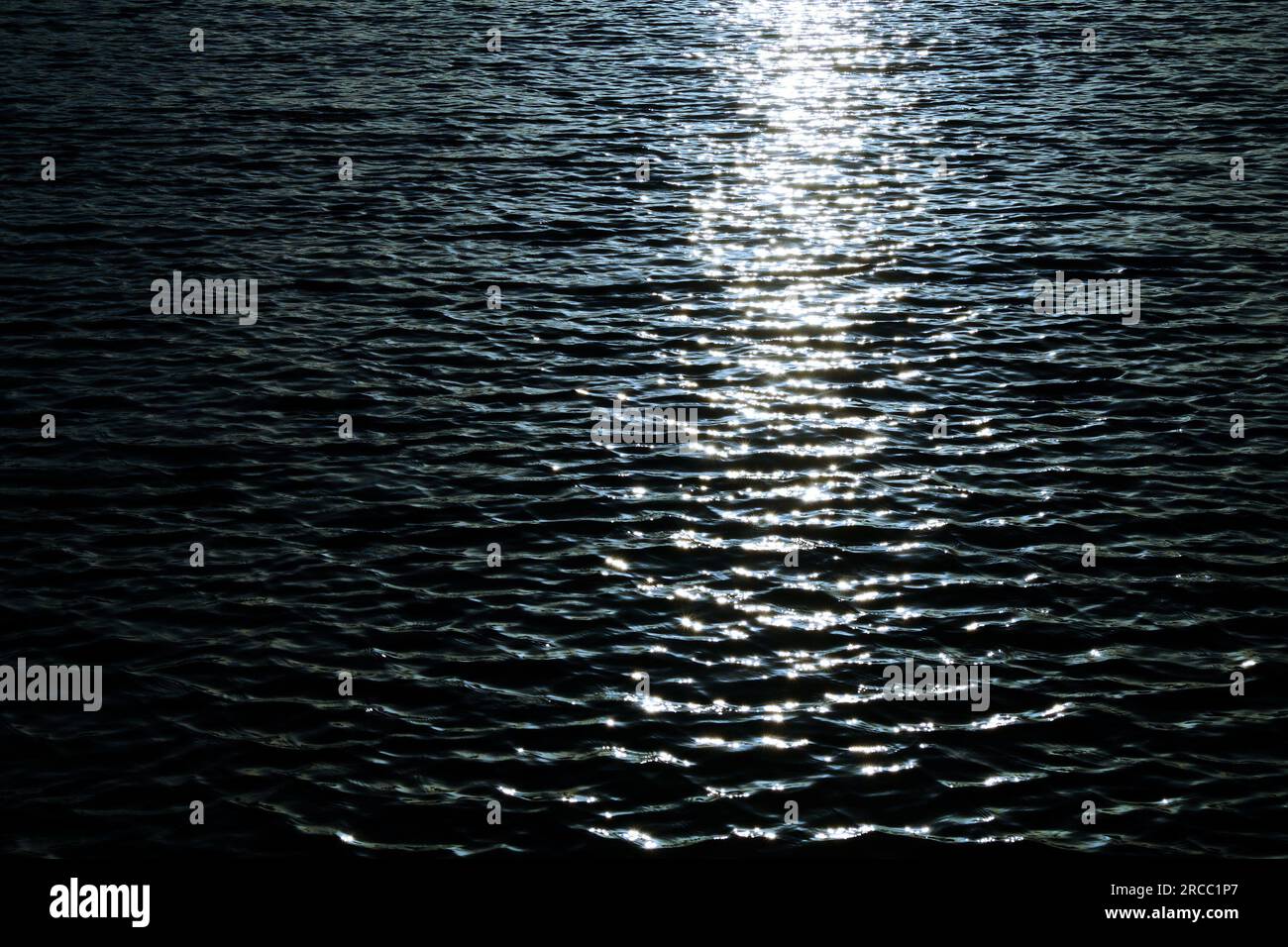 Rippled water surface with sun path reflections, dark tone image with high contrast. Stock Photo