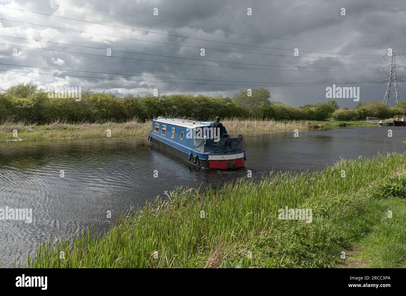long House boat turning around on a canal against a stormy sky Stock Photo