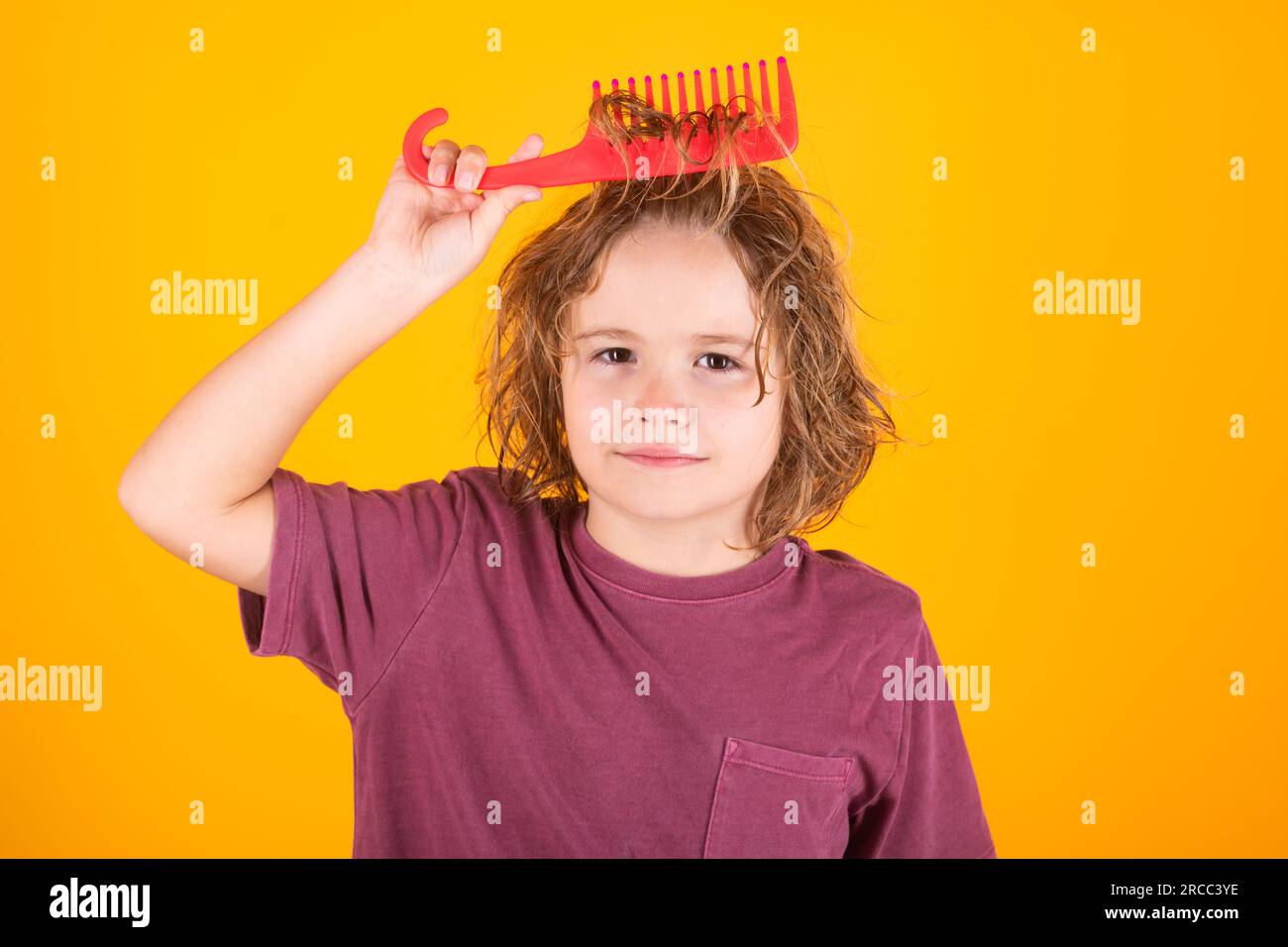 Cute child with curly blonde hair holding comb hairbrush for combing