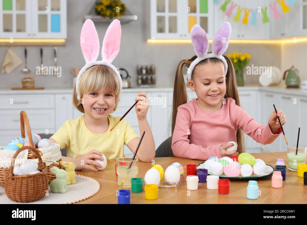 Children painting Easter eggs at table in kitchen Stock Photo