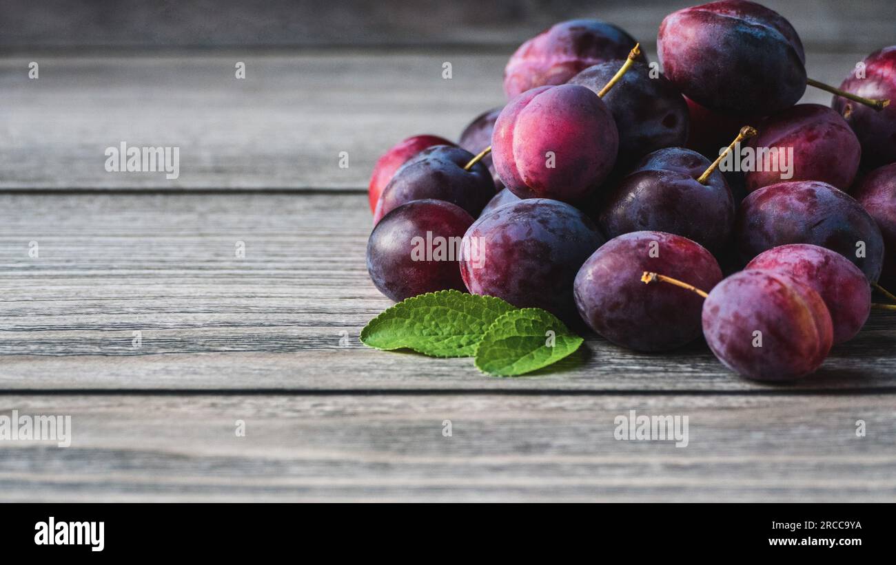 Plums on wooden table, harvested prune fruits green leaves in a pile closeup, copy space Stock Photo