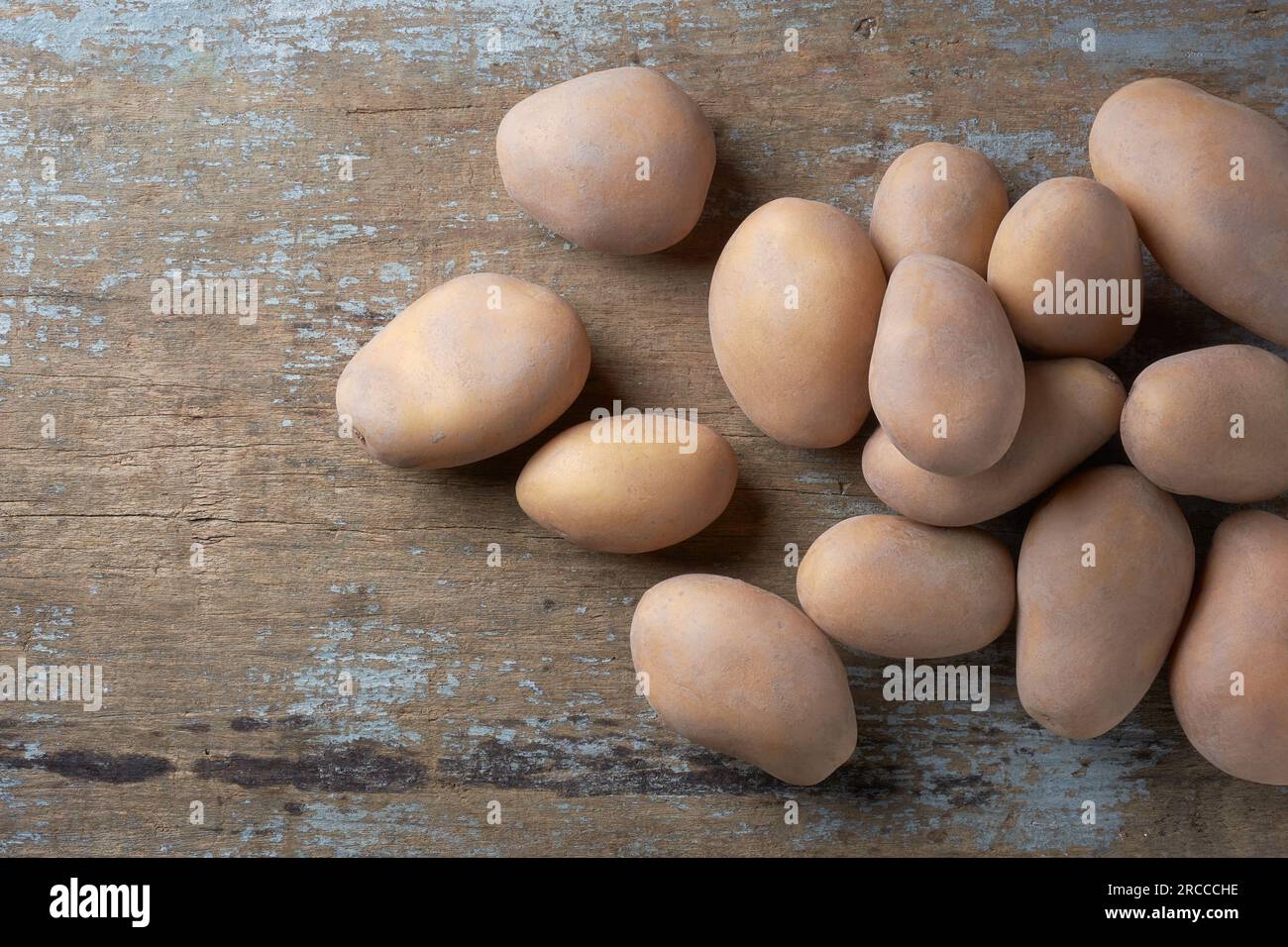 pile of freshly harvested raw potatoes, solanum tuberosum, starchy, tuberous vegetables scattered on wooden table top, taken straight from above Stock Photo