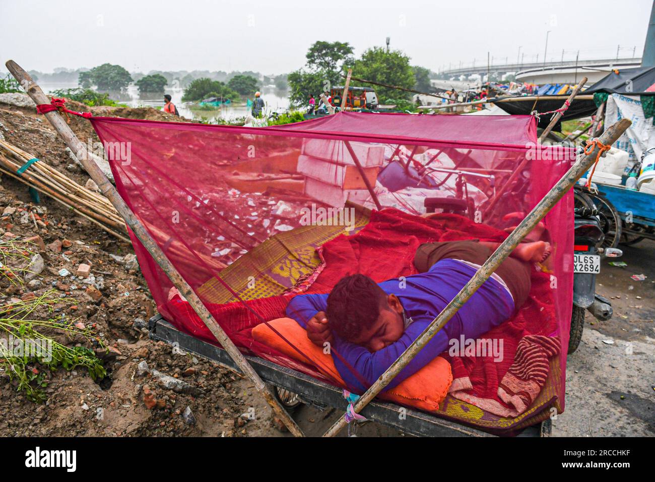 New Delhi, India. 12th July, 2023. A man sleeps in a mosquito net on the street after being displaced by the rising water level of the Yamuna River following heavy monsoon rains in New Delhi. Yamuna water level in Delhi reaches all-time high of 207.55 meters. The government warned of flood-like conditions and asked residents of the riverbed and low-lying areas to evacuate their homes. Credit: SOPA Images Limited/Alamy Live News Stock Photo