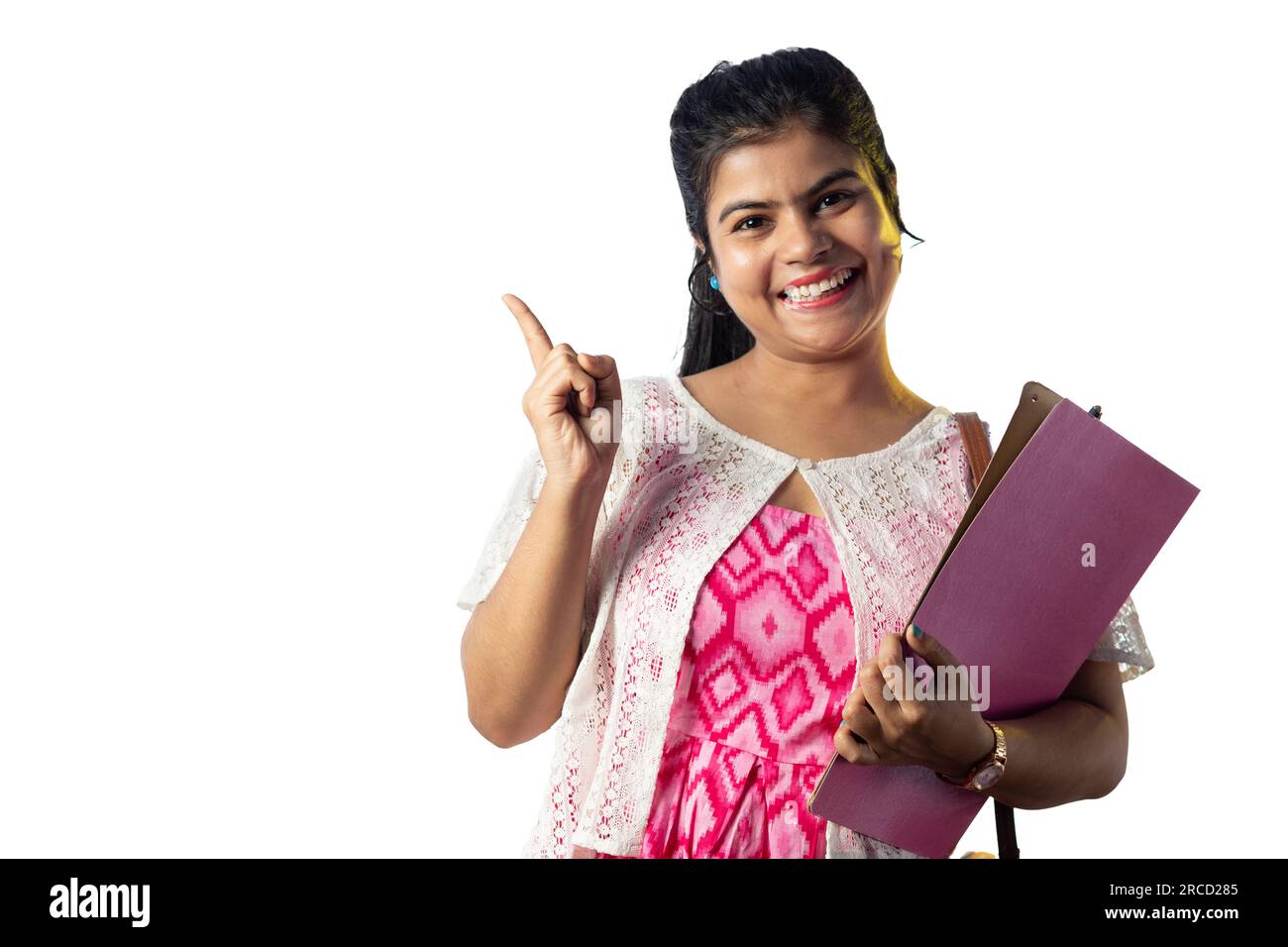 A pretty young Indian girl with books in hand pointing with smiling ...