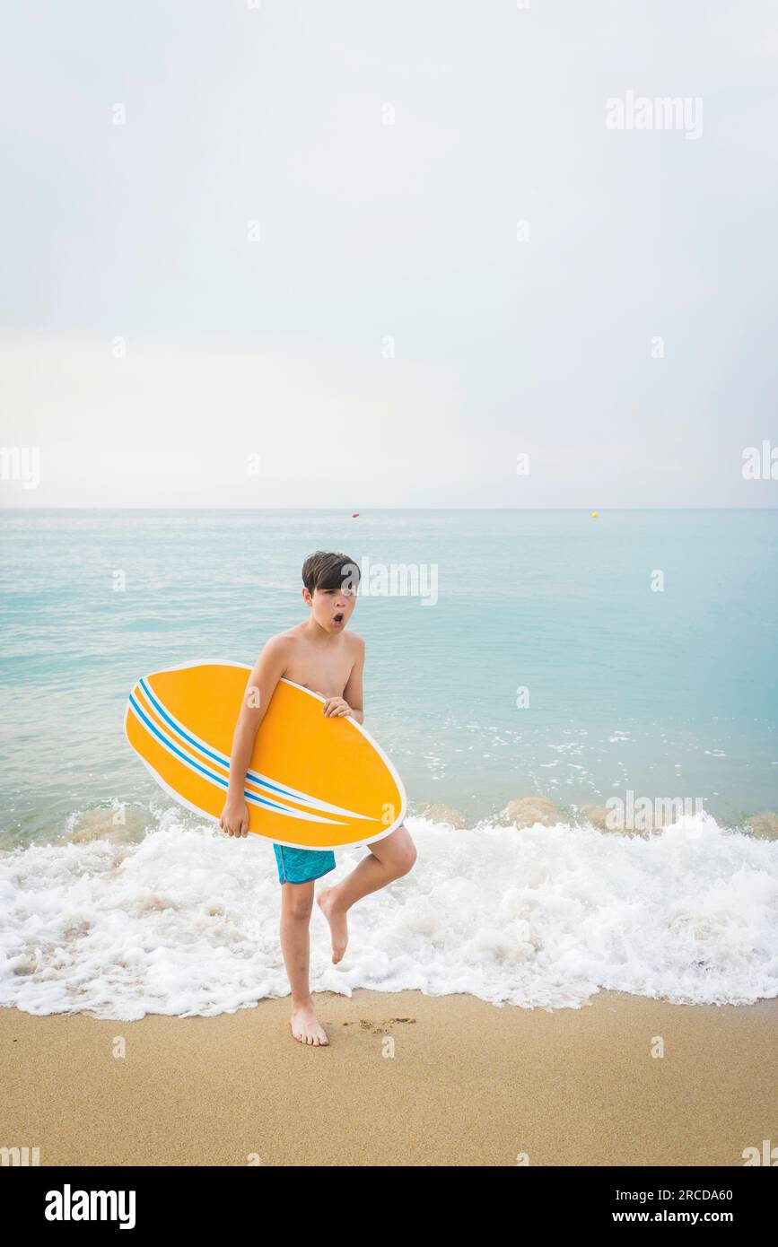 Portrait of a joyful smiling teen boy with yellow surfboard standing on the beach Stock Photo