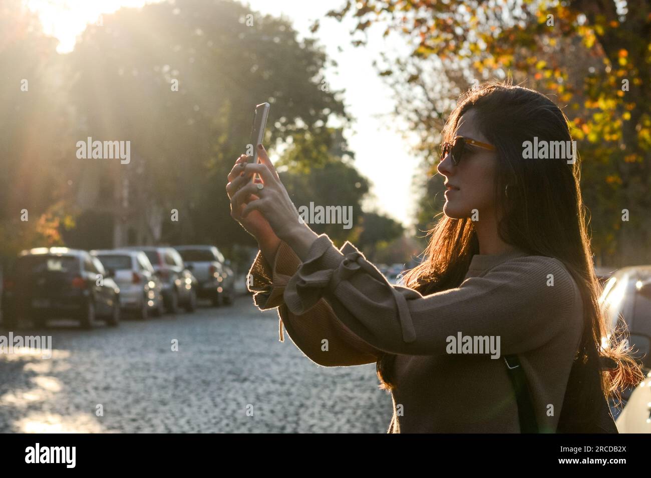 Side view of young woman photographing while standing on the street Stock Photo